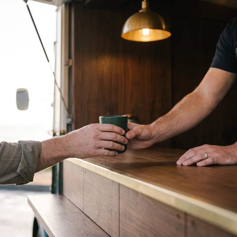 Two hands meeting over the counter as a green stoneware cup changes hands.