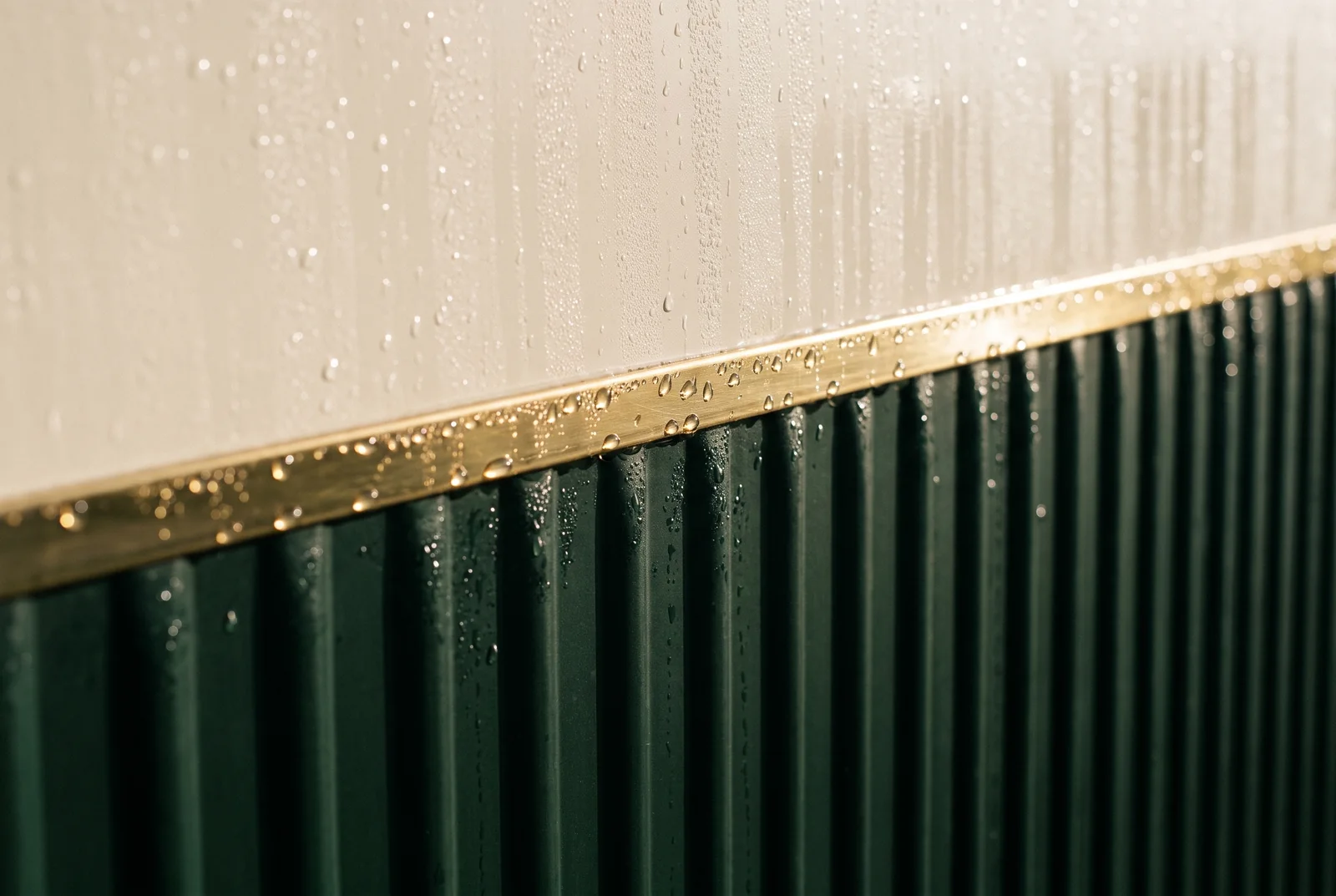 Extreme close-up of the brass pinstripe where the cream paint meets the bottle-green corrugated steel.